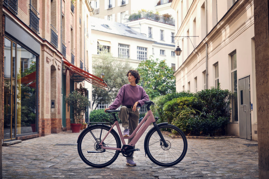 Young Woman on Cobblestone Street Standing WIth Riese & Muller Culture Mixte E-Bike in Colour Blossom 