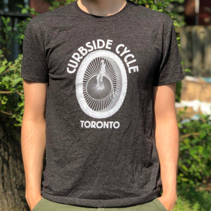 Curbside Cycle Old School Logo T-Shirt with Bike Wheel in Colour Black on Male Model Outside in the Sun