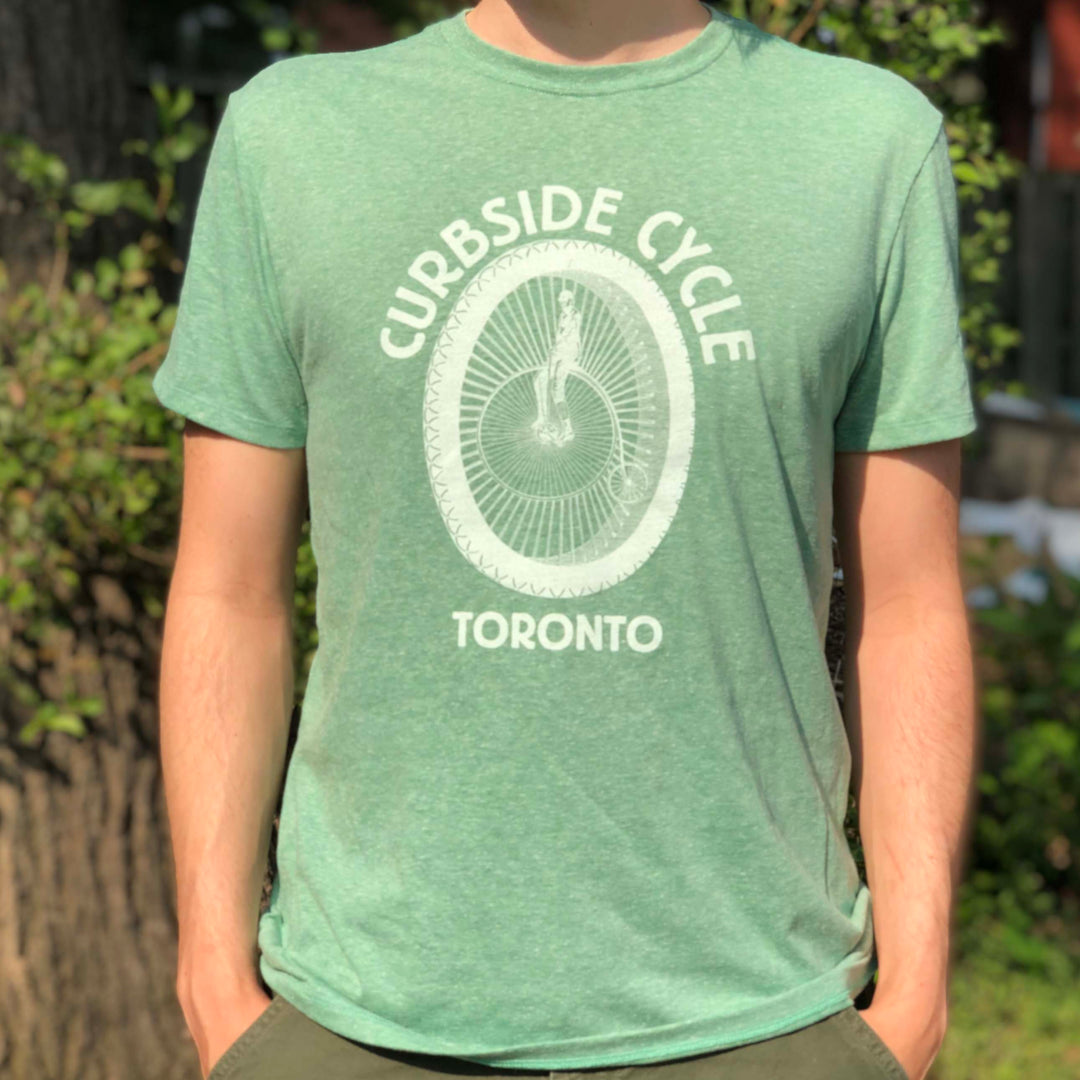 Curbside Cycle Old School Logo T-Shirt with Bike Wheel in Colour Green on Male Model Outside in the Sun