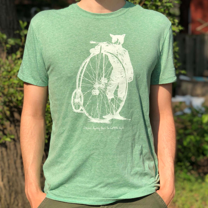 Curbside Cycle 'Cat With Penny-Farthing Bike' T-Shirt in Colour Green on Male Model Outside in the Sun