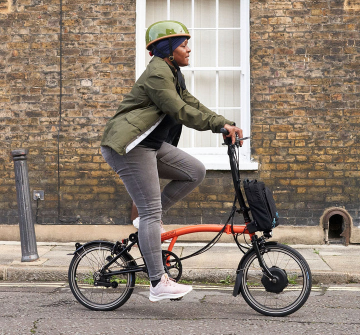 Woman riding a Brompton Electric C Line Explore High Handlebar in Fire Coral