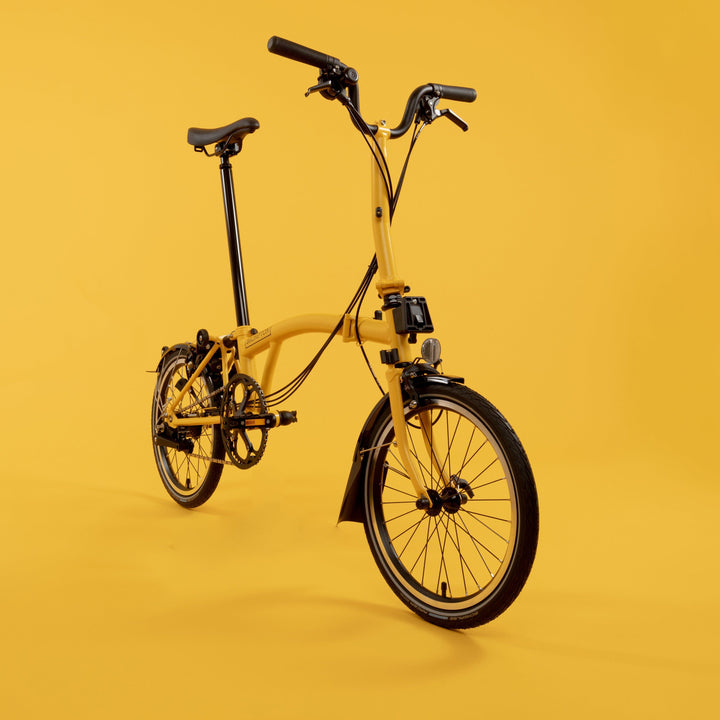 Brompton Folding Bike in Bright Bumblebee Yellow Colour with a Mid Handlebar Facing Straight in front of Yellow Background