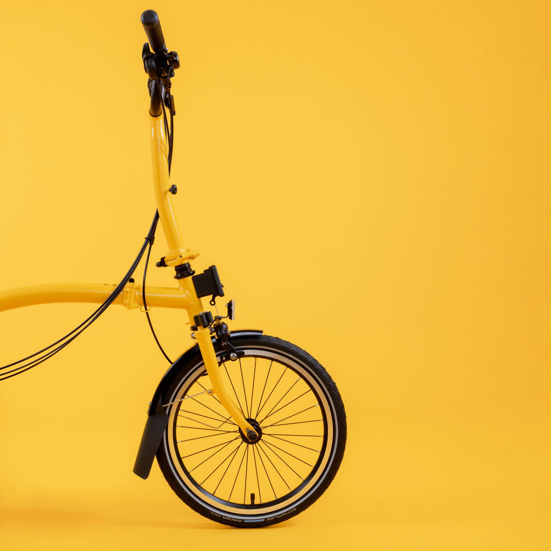 Front Half of Brompton Folding Bike in Bright Bumblebee Yellow Colour with a Mid Handlebar with Front Carrier Block on Yellow Background