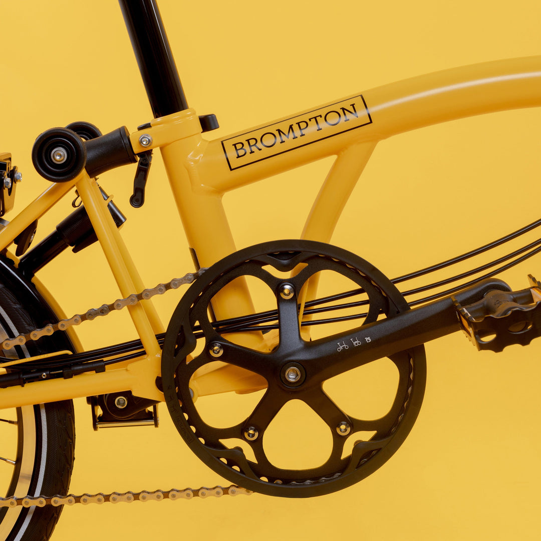 Crankset and Lower Frame of Brompton British Folding Bike in Bright Bumblebee Yellow Colour with a Mid Handlebar on Yellow Background