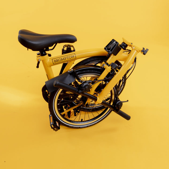 Folded Brompton C Line Bike in Bumblebee Yellow with Low Handlebar on Yellow Background