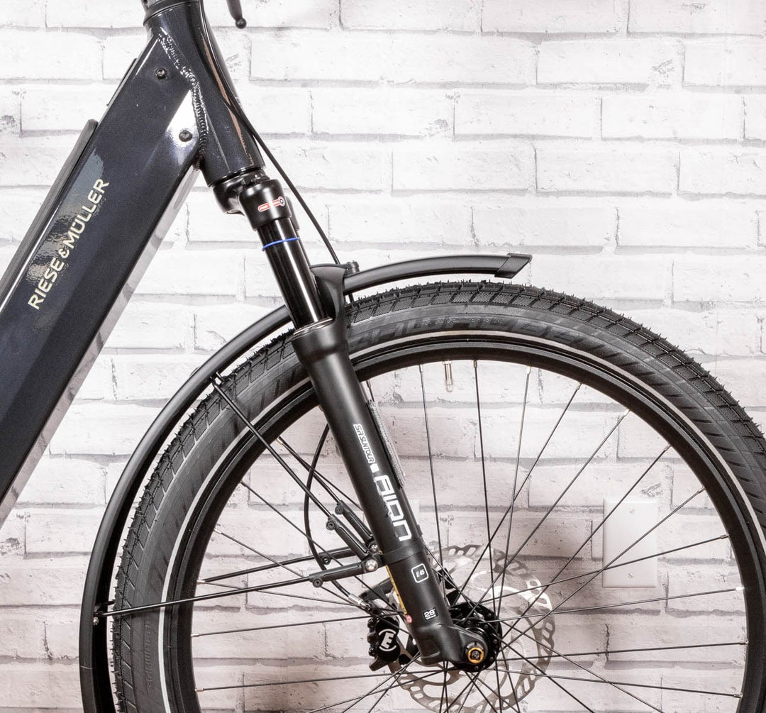 Front detail of suspension fork front end of R&M Nevo 3 GT Rohloff in Lunar Grey Metallic 47cm against a fake break wall studio shot.